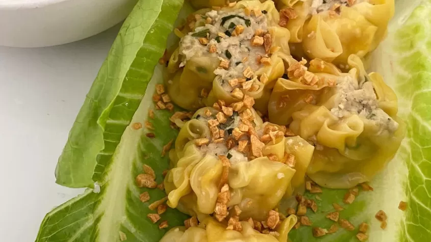 image of dumplings on lettuce leaves with seasoning on top and soy sauce in a dish