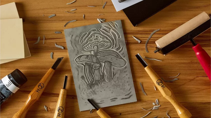 wooden table with wooden handled carving tools and a piece of foam with mushrooms carved out of it