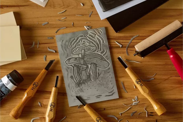 wooden table with wooden handled carving tools and a piece of foam with mushrooms carved out of it
