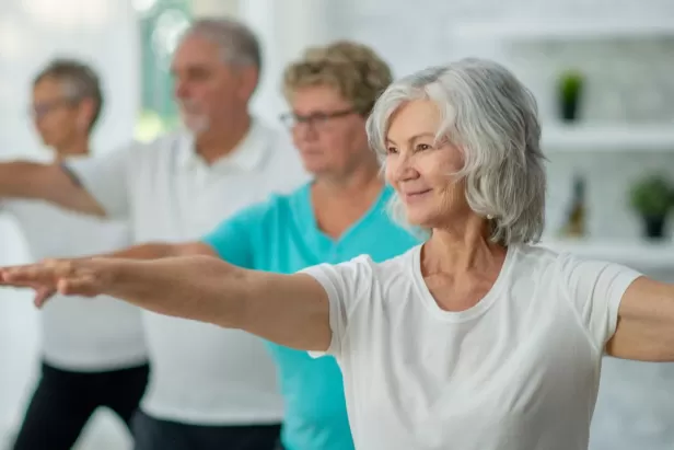 older humans in a yoga pose with their arms stretching forward and back
